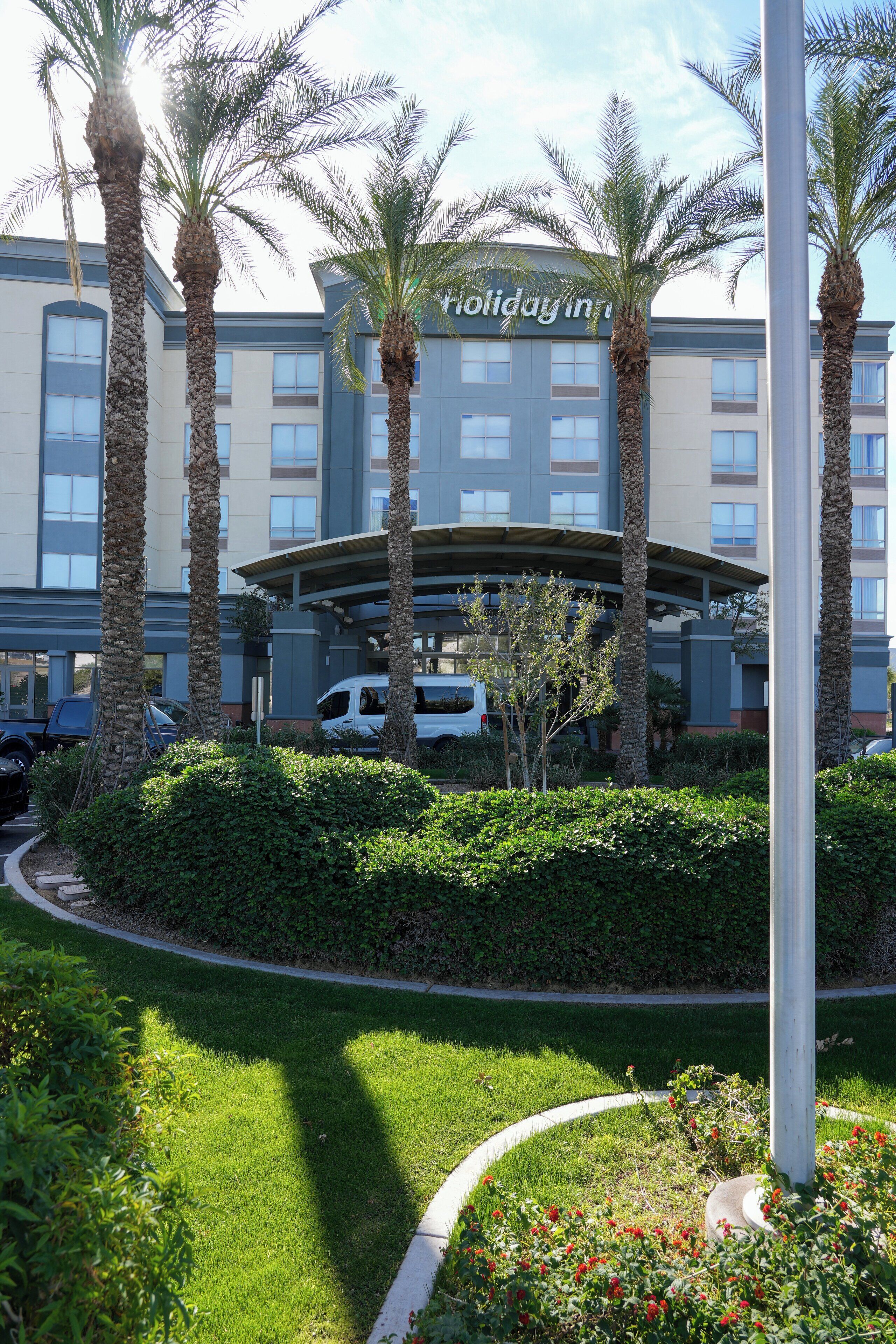 A hotel with a modern design, palm trees, and a well-maintained lawn.