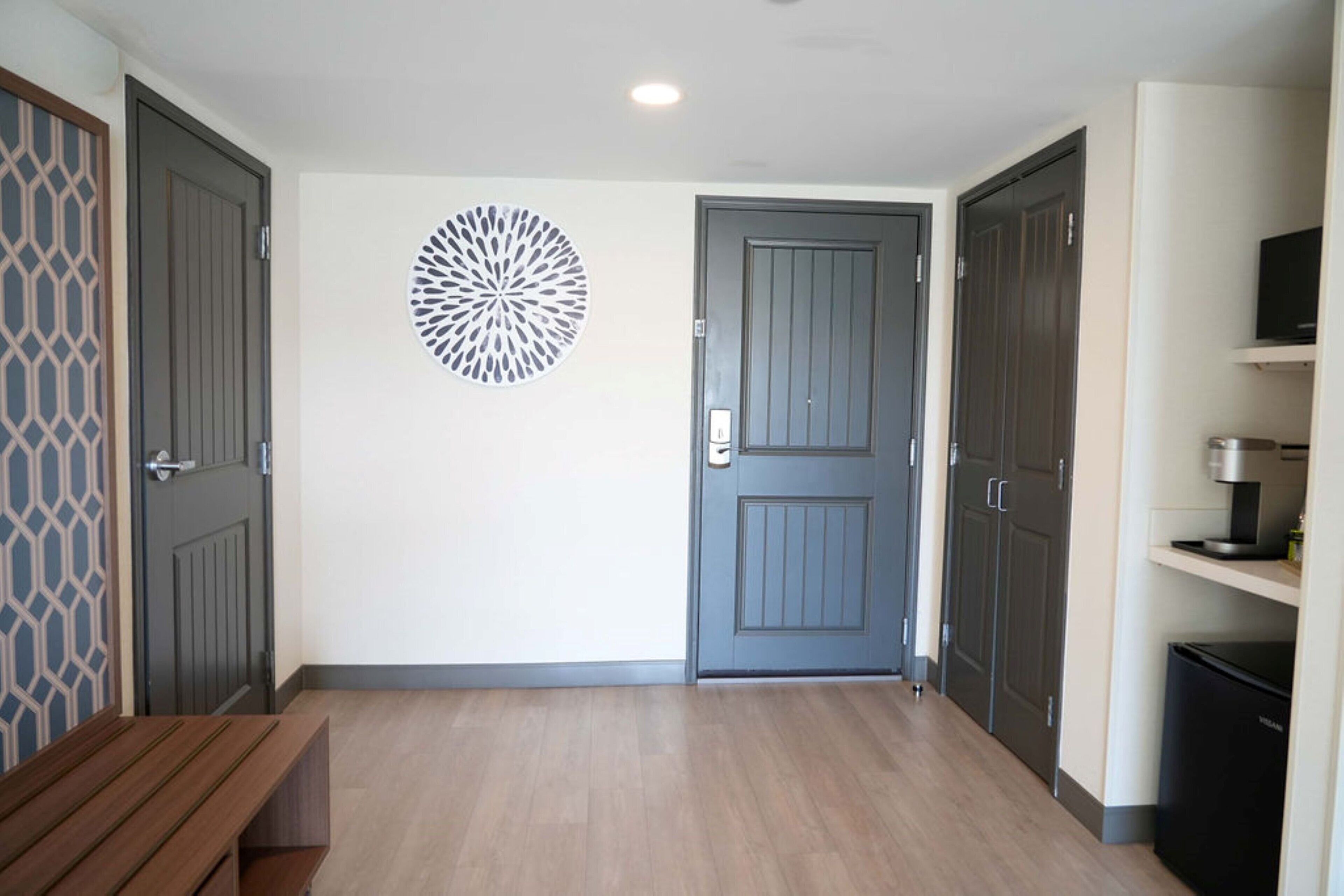 Un couloir avec un banc en bois, une porte grise et un élément décoratif fixé au mur.