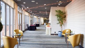 A hotel corridor with tables and chairs, string lights, and a potted plant. - Holiday Inn Hotel & Suites PHOENIX AIRPORT by IHG (Phoenix)