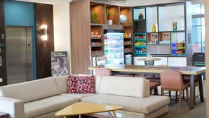 A modern hotel lobby with a sofa, a small table, a refrigerator, a vending machine, and a coffee station. - Holiday Inn Hotel & Suites PHOENIX AIRPORT by IHG (Phoenix)