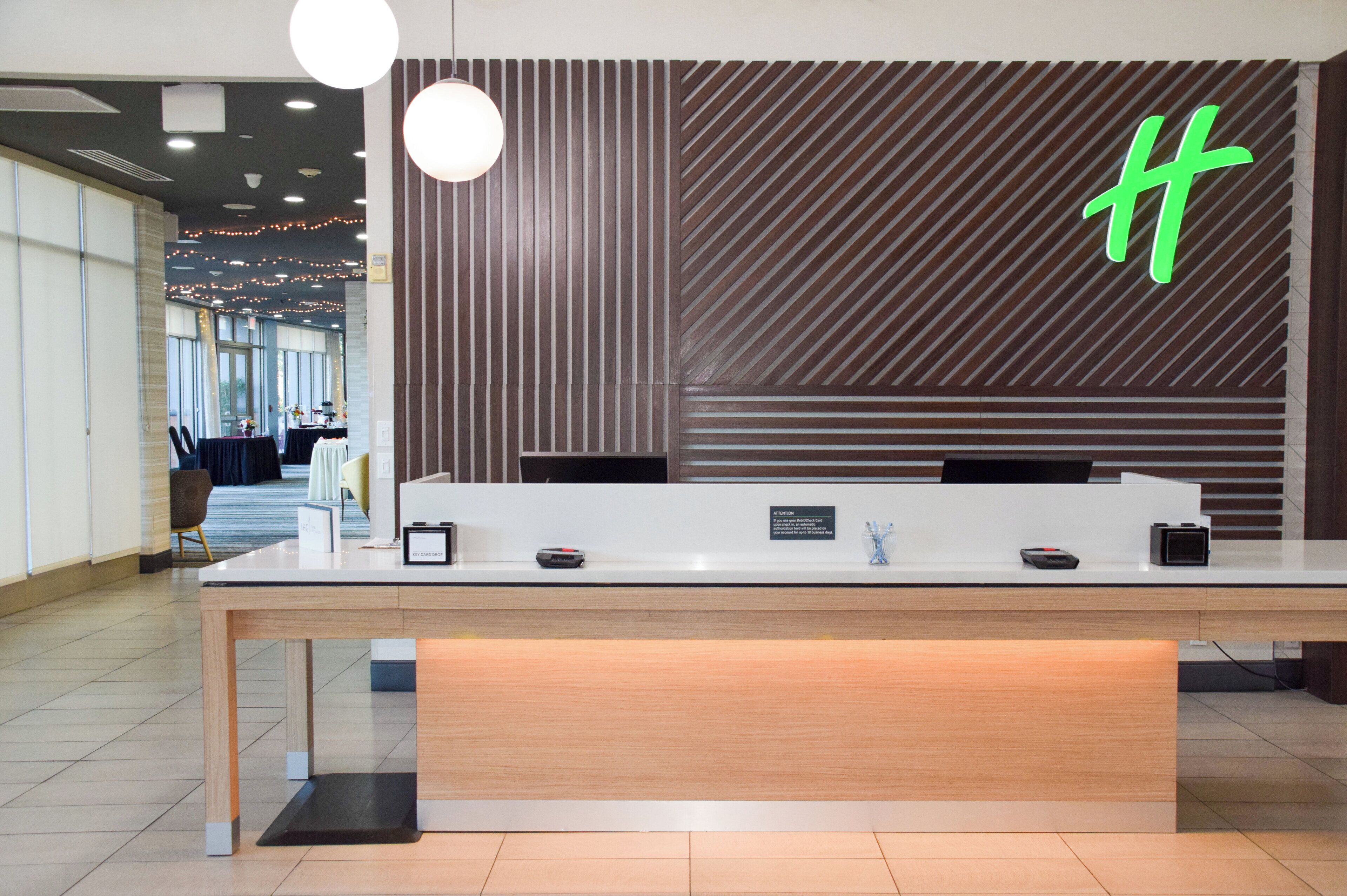 A reception desk with a modern design, featuring a wooden panel wall with a geometric pattern and a neon sign.