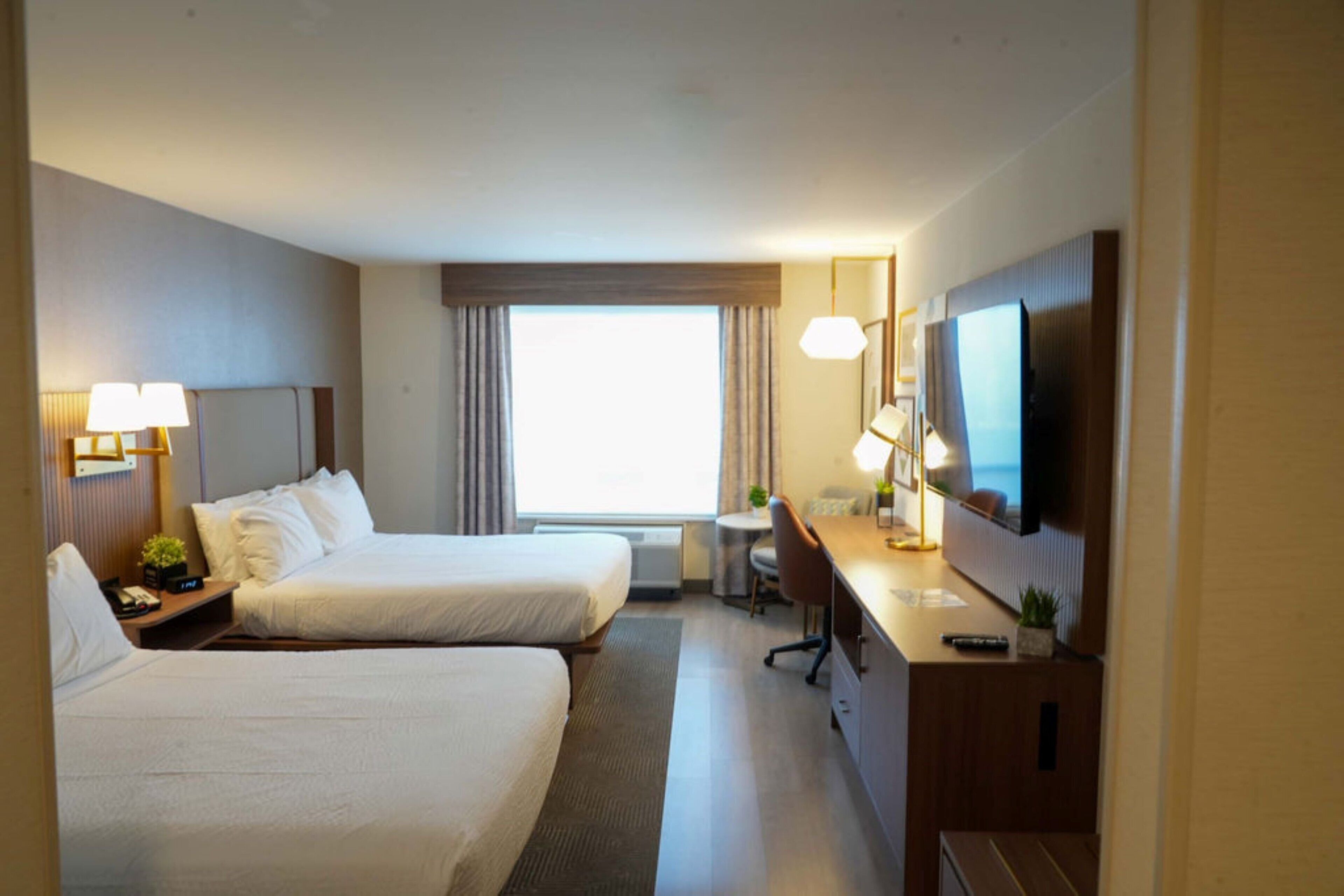 Une chambre d’hôtel avec deux lits, un bureau, une télévision et une fenêtre avec des rideaux.