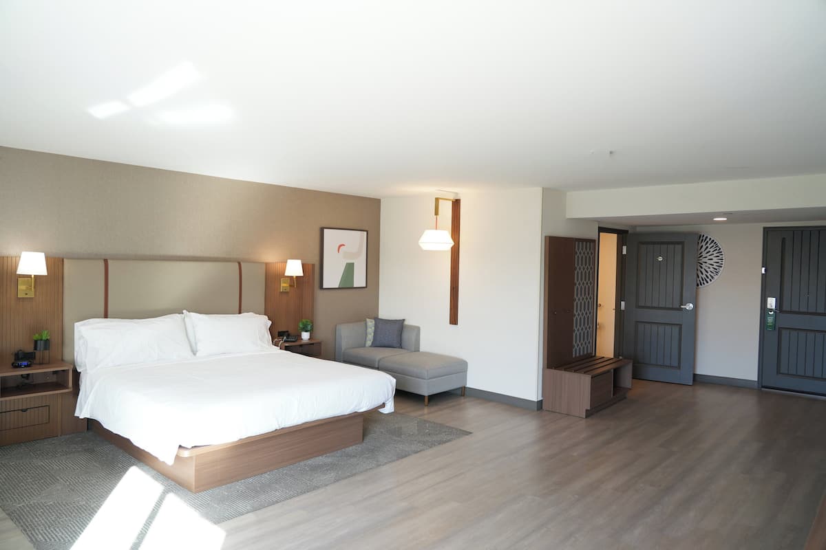 A hotel room with a large bed, bedside tables, a sofa, a desk, and a door with a decorative panel.