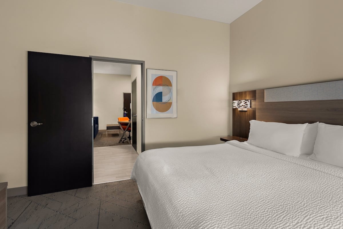 Hotellihuone, jossa on suuri sänky, ovi, joka johtaa käytävään, ja seinällä oleva kehystetty taideteos.