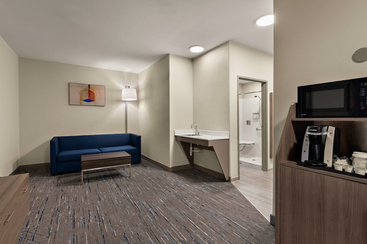 Hotellihuoneessa on sininen sohva, pieni pöytä, mikroaaltouuni, kahvinkeitin ja pesuallas.
