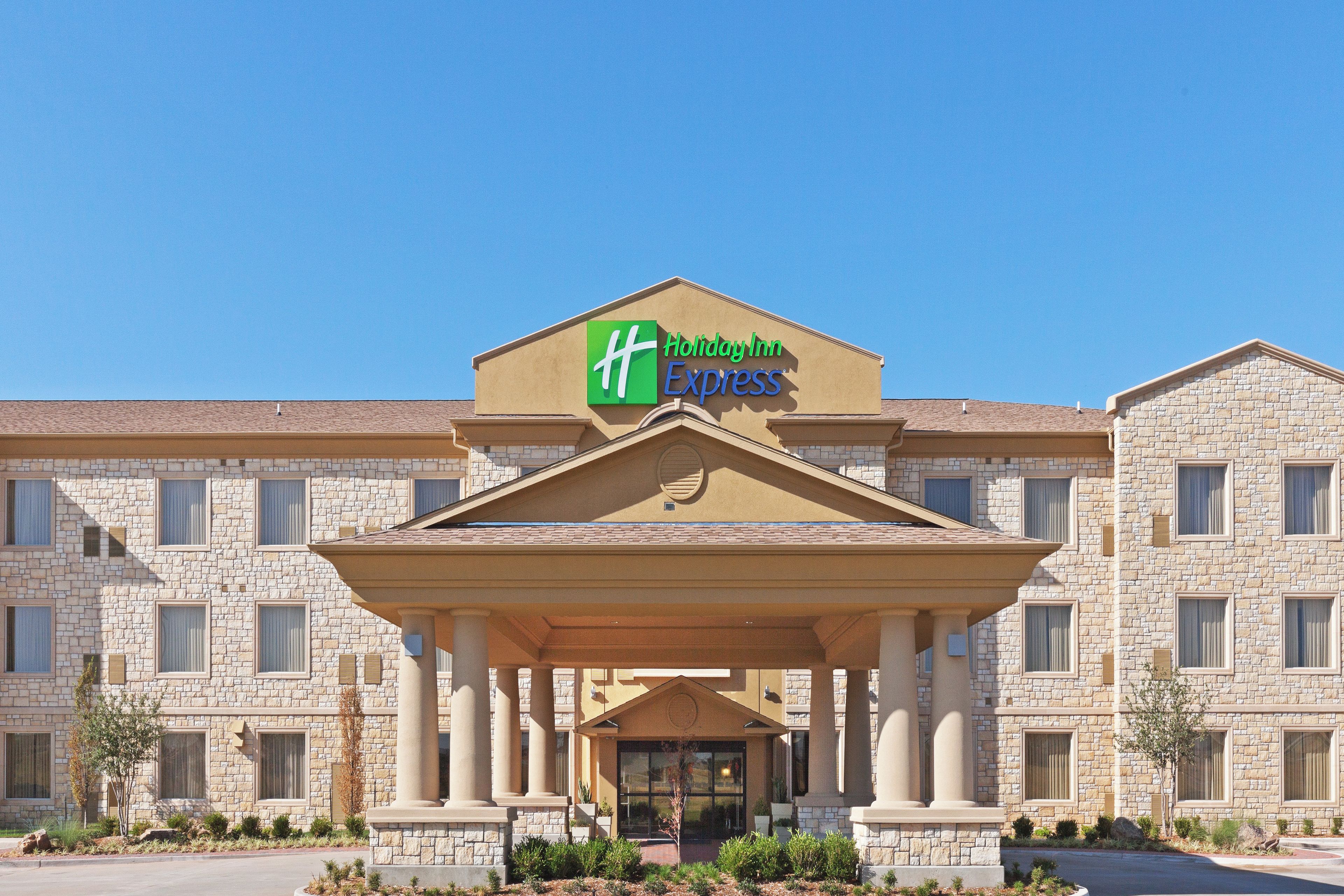 A Holiday Inn Express building with a stone facade, a central entrance with columns, and a clear blue sky above.