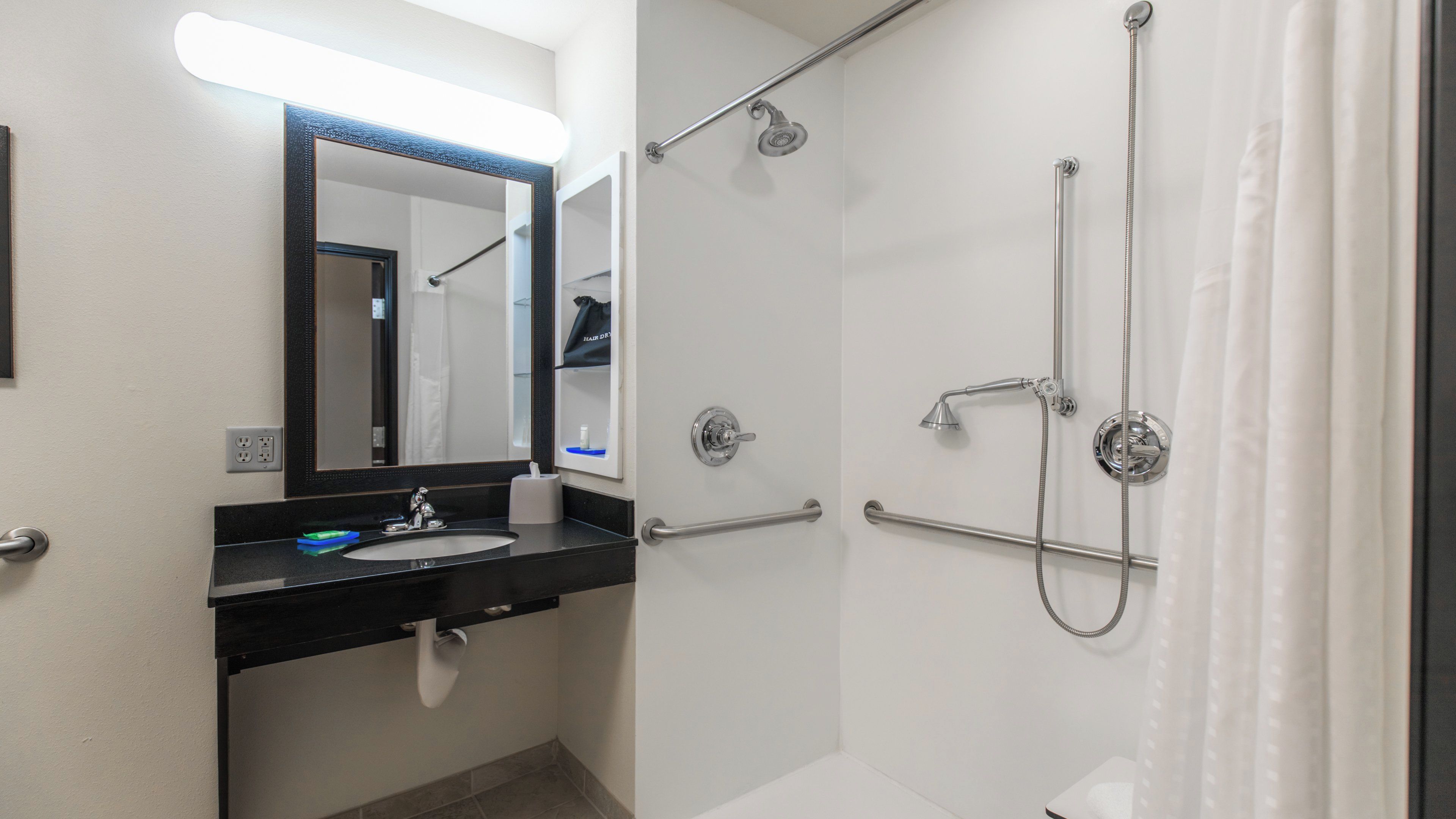 A bathroom with a sink, mirror, shower, and handrails.