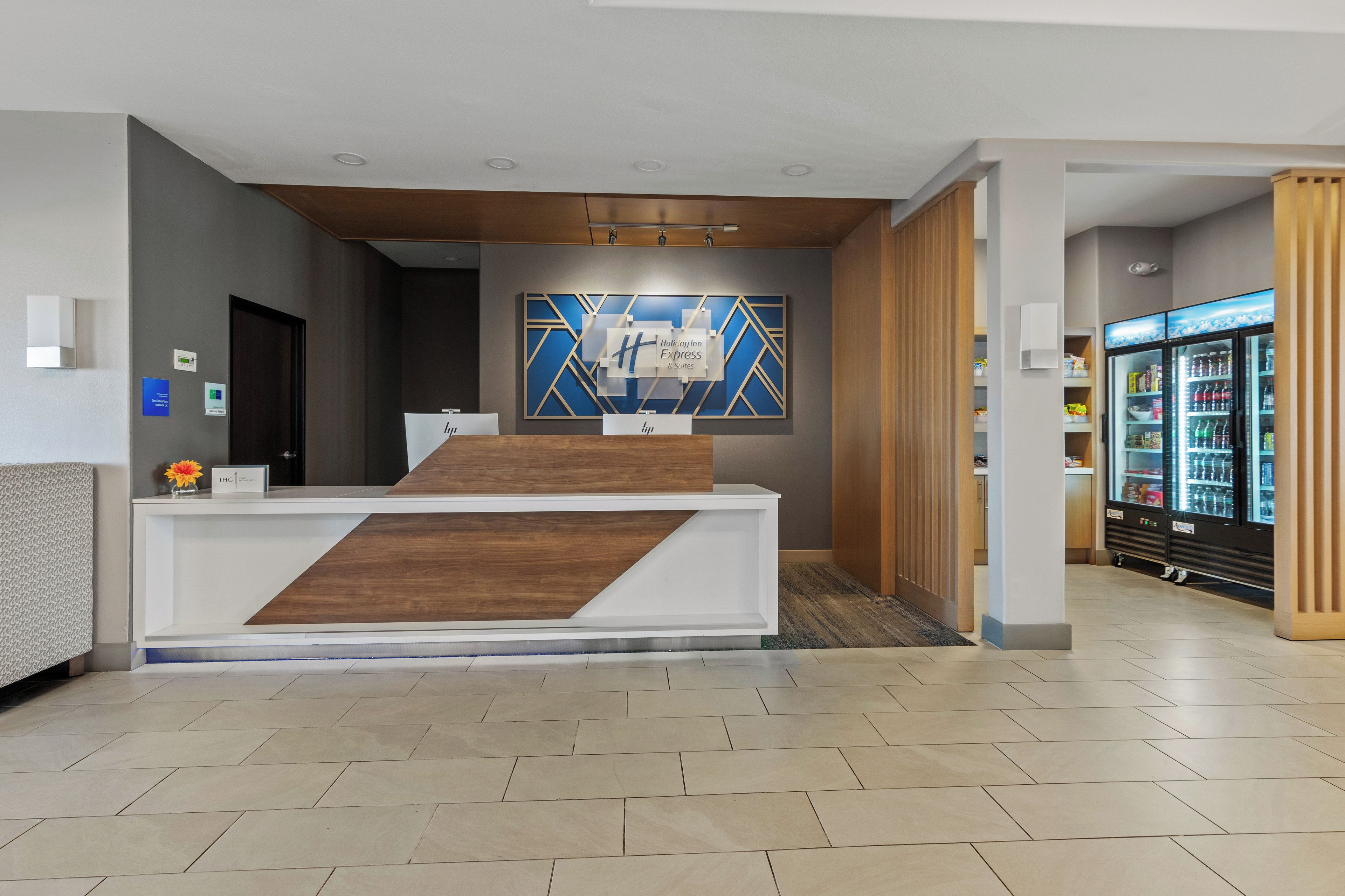 A hotel reception desk with a modern design, a wall-mounted sign, and a refrigerator stocked with beverages.