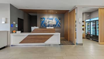 A hotel reception desk with a modern design, a wall-mounted sign, and a refrigerator stocked with beverages.