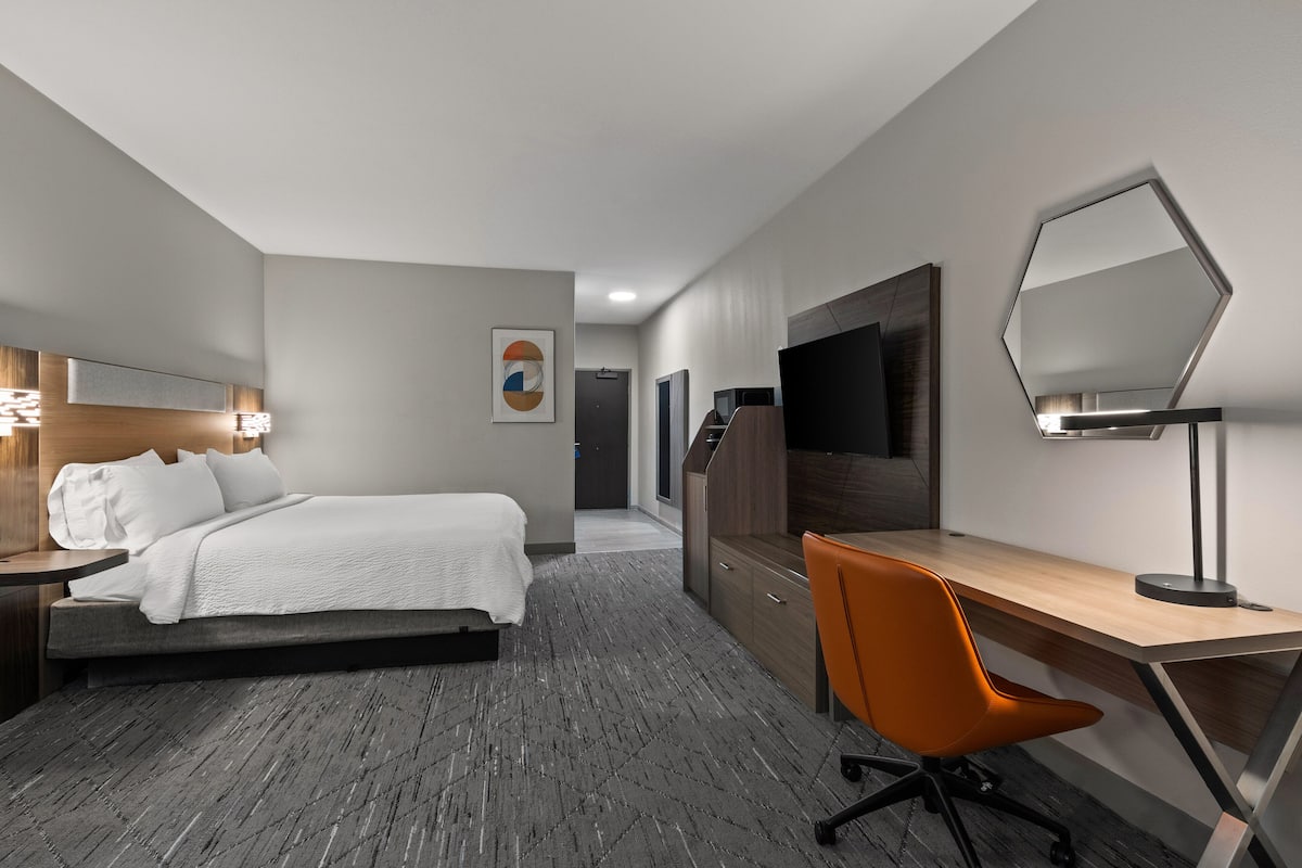 Moderni hotellihuone, jossa on sänky, työpöytä, tuoli ja suuri peili.