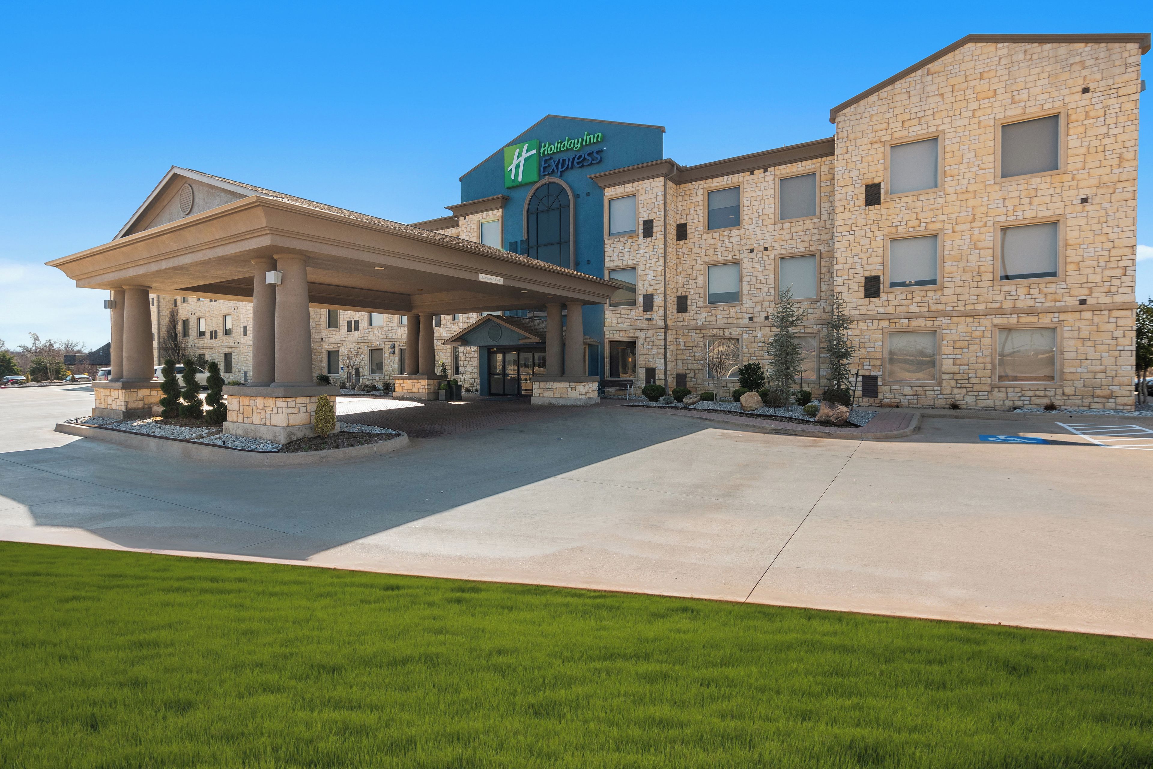 A Holiday Inn Express hotel with a covered entrance, a parking lot, and a landscaped area with shrubs.