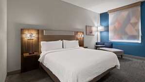 A modern hotel room with a large bed, bedside tables, a nightstand, a small table, a chair, and a large window with geometric blinds. - Holiday Inn Express & Suites Oklahoma City NW-Quail Springs by IHG (Oklahoma City)