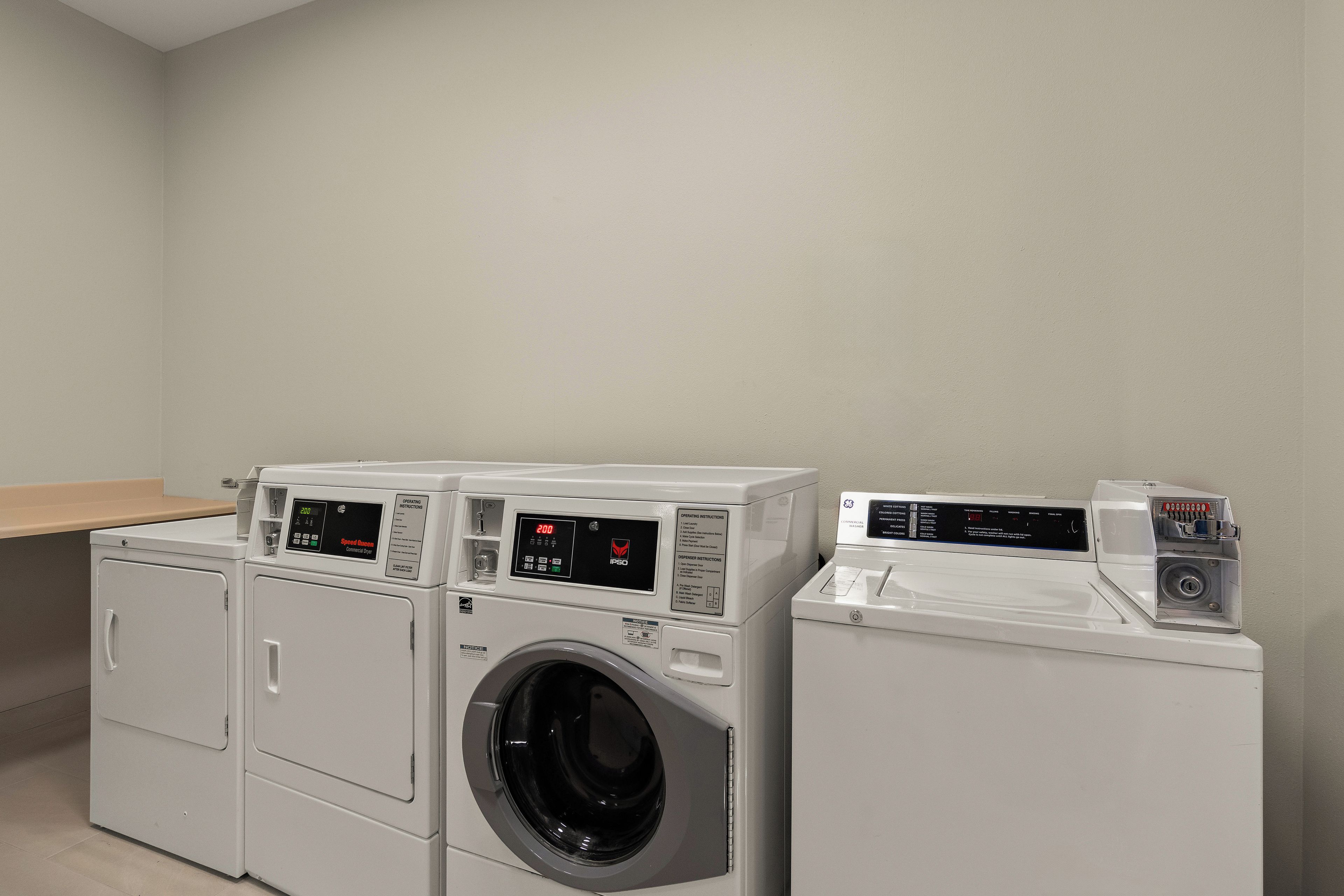 A laundry area with two front-loading washers and a dryer, a bench, and a wall-mounted dispenser.