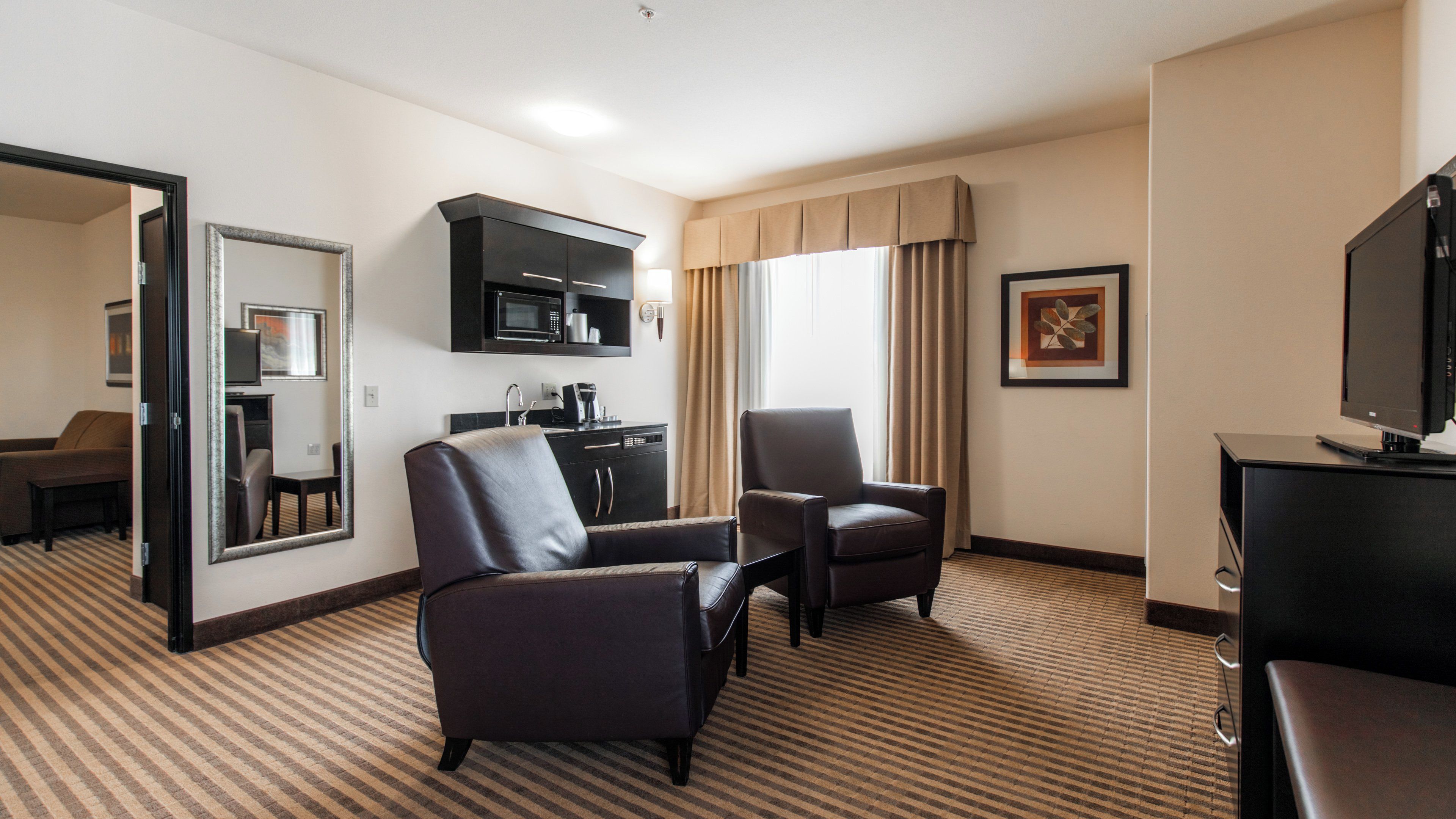 Ein Hotelzimmer mit Sofa, Sessel, Fernseher und einer Küchenzeile.