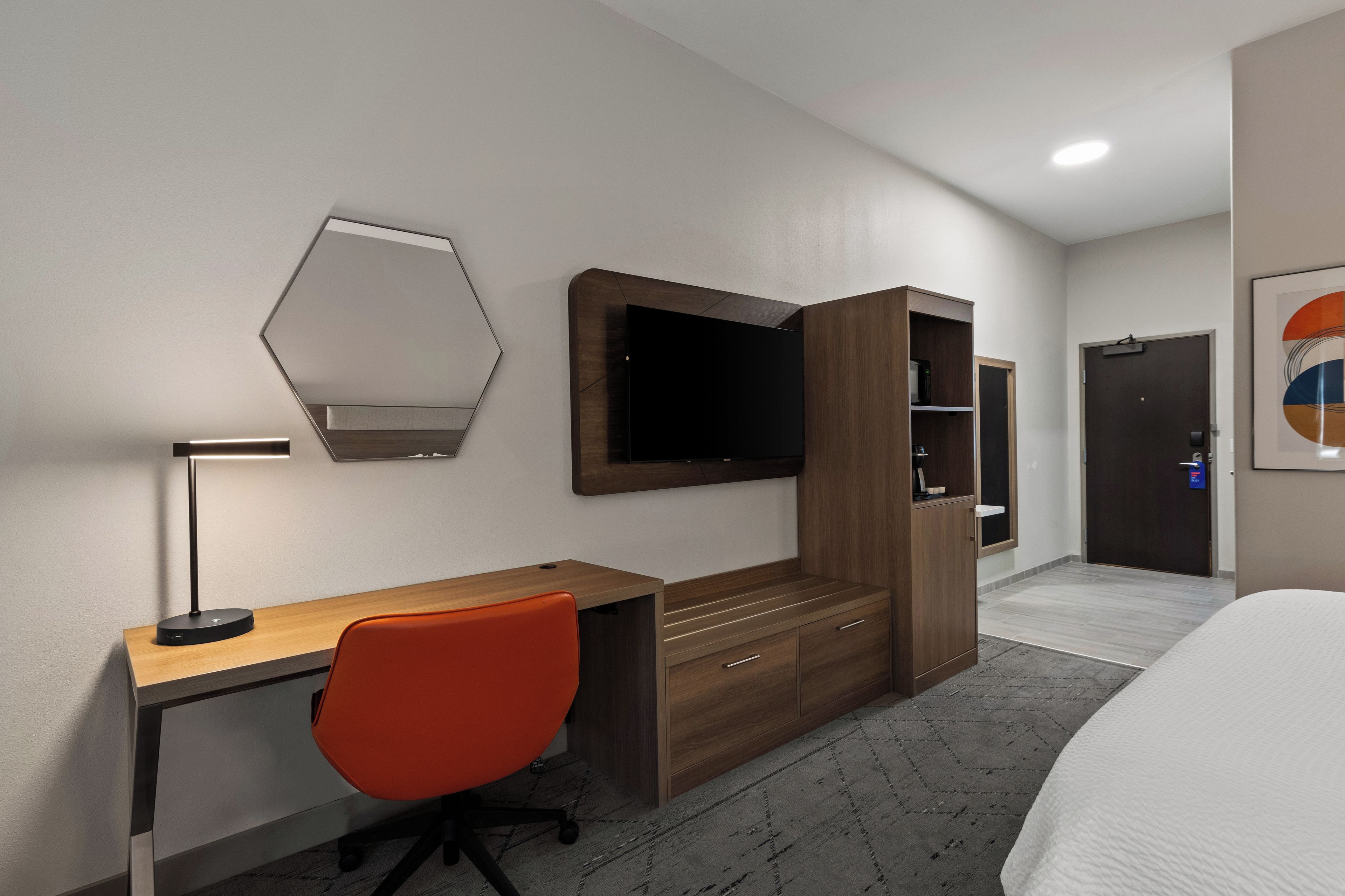 Habitación de hotel con escritorio de madera, una silla roja, televisor de pantalla plana en la pared, armario y una cama.