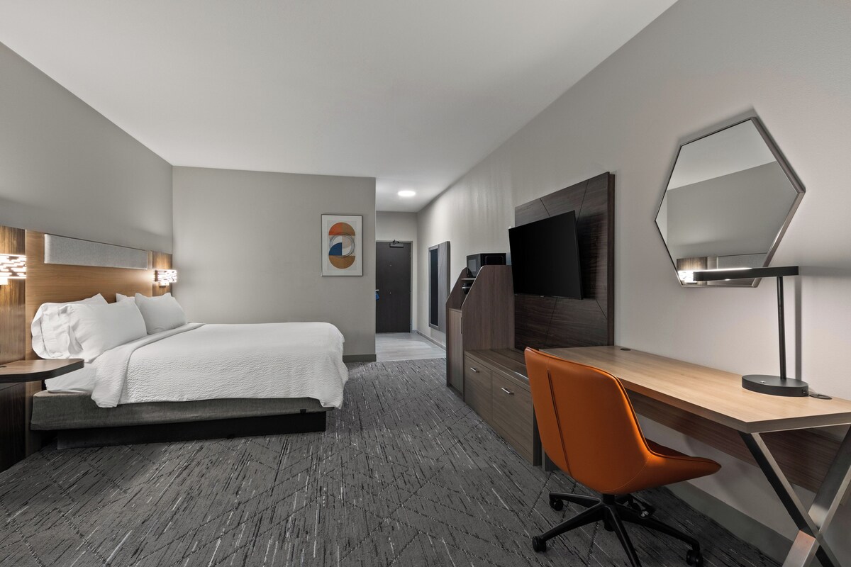 A modern hotel room with a bed, desk, chair, and a large mirror.