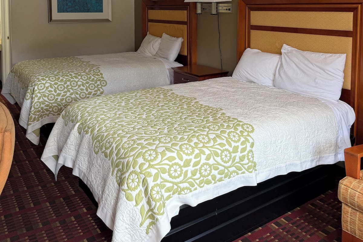 A hotel room with two beds, a nightstand, a lamp, and a painting on the wall.