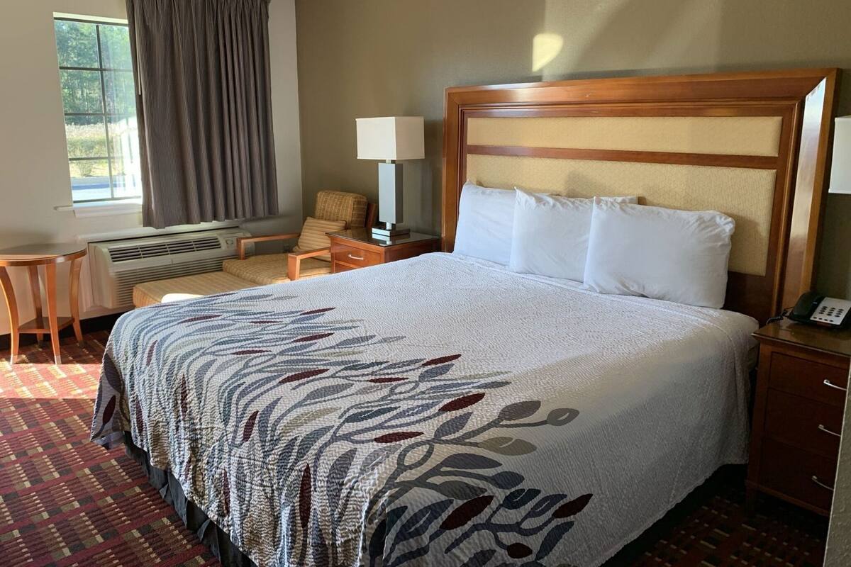 A hotel room with a large bed, a chair, a desk, a lamp, and a telephone.