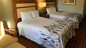 Habitación de hotel con dos camas, una mesita de noche, una lámpara, una silla y un cuadro en la pared.