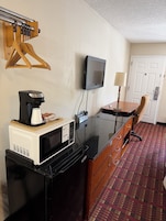 A compact hotel room with a kitchenette, a television, a desk, and a chair.