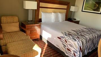 A hotel room with a bed, a chair, a nightstand, and a lamp.