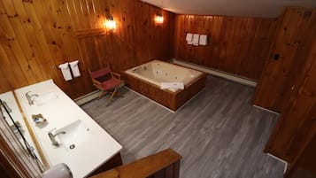 Baño de cabaña de madera con lavamanos, espejo y bañera de madera.