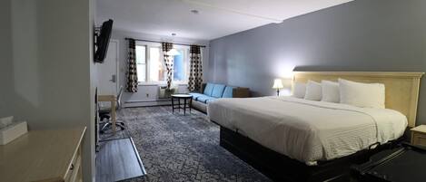 A hotel room with a large bed, a desk, a chair, a sofa, and a TV mounted on the wall.