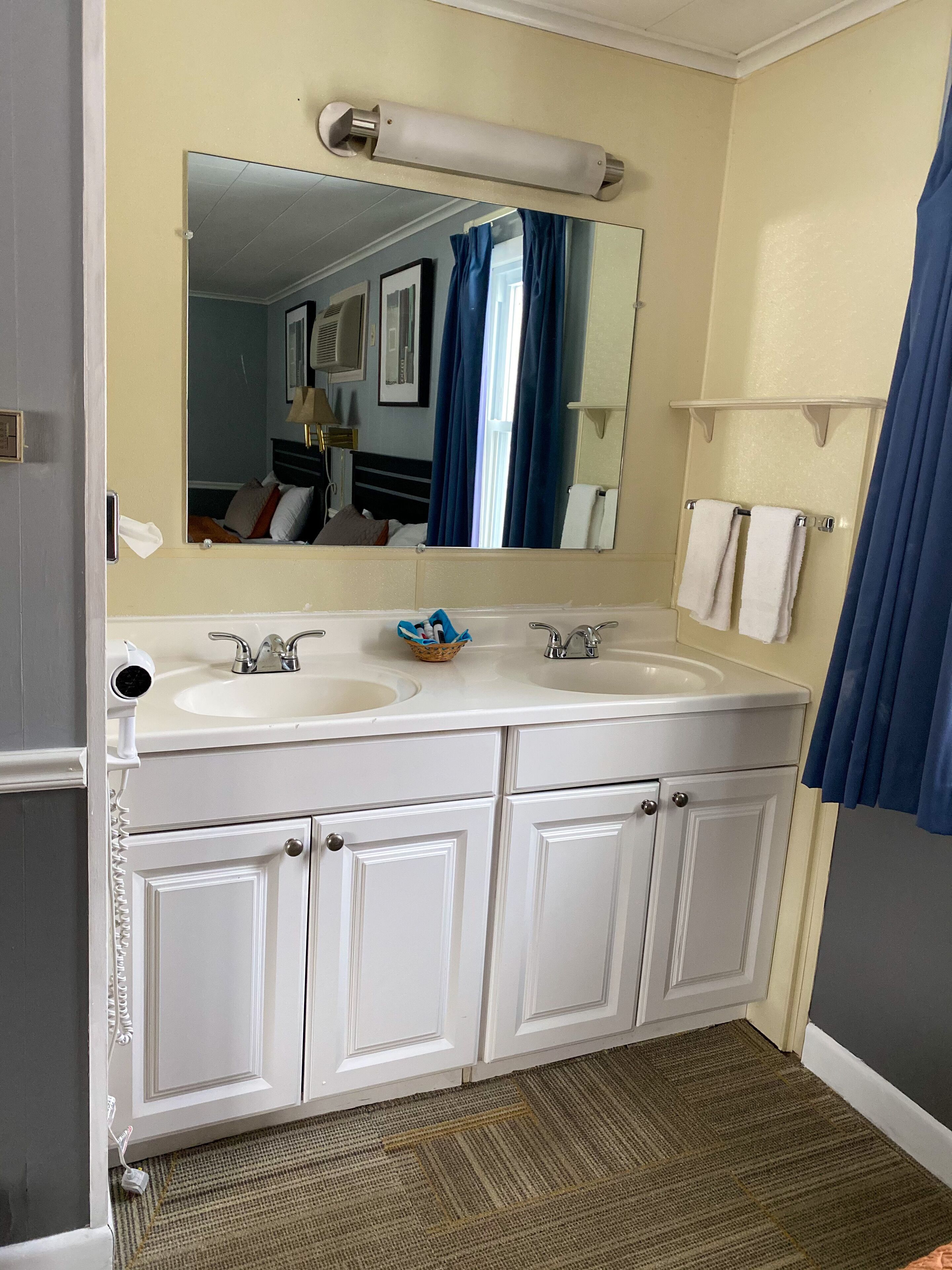 Une salle de bain avec deux lavabos, un miroir, un porte-serviettes et un rideau de douche.
