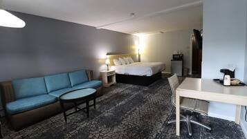 Habitación de hotel con sofá azul, cama, escritorio con silla y pequeña mesa con cafetera.