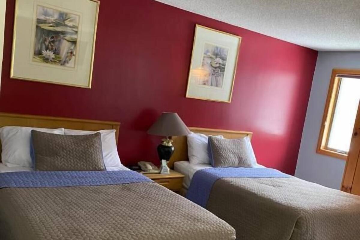 Ein Hotelzimmer mit zwei Betten, roten Wänden und gerahmten Kunstwerken.