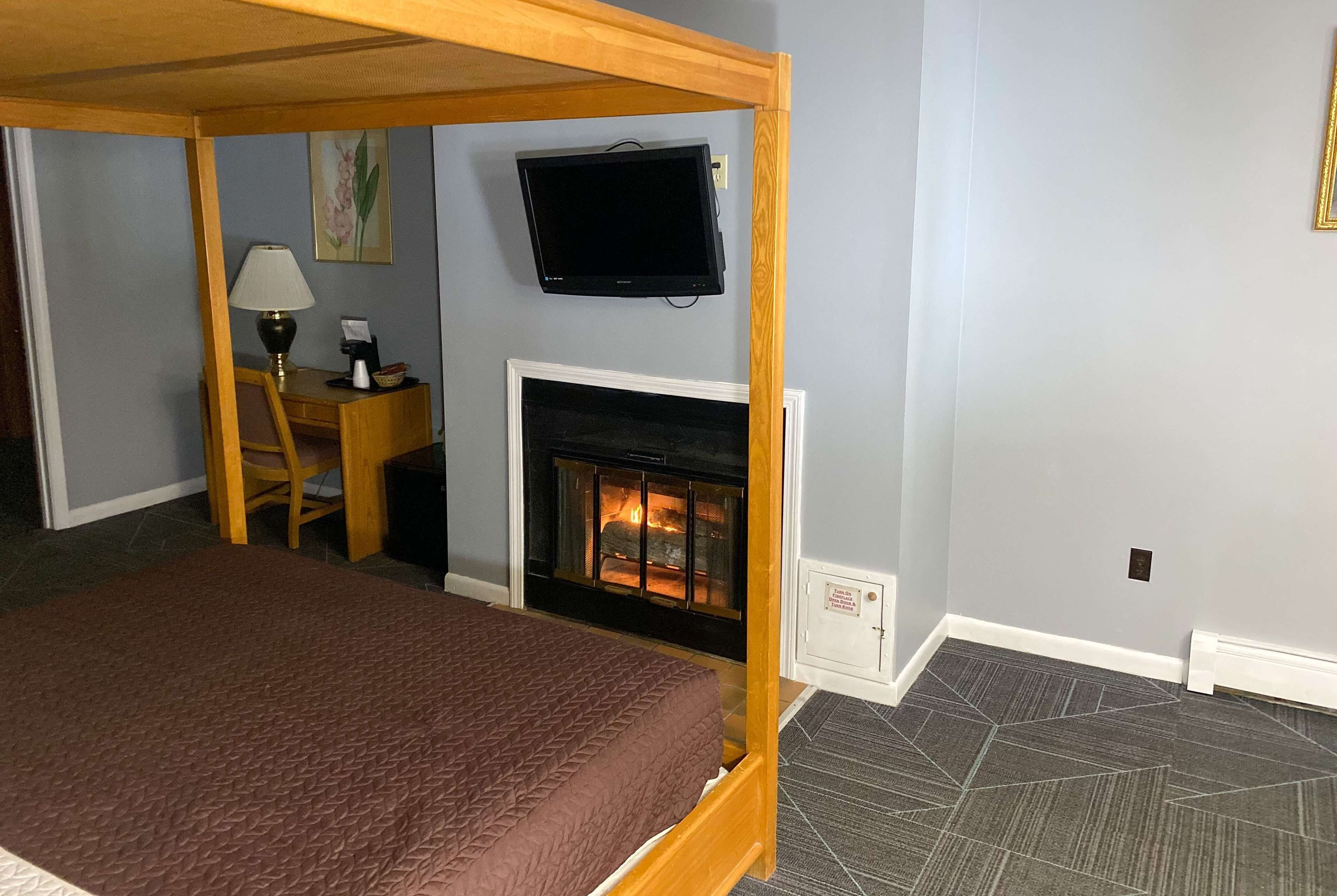 Un dormitorio con cama, escritorio, silla, televisor y chimenea.