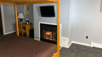 Un dormitorio con cama, escritorio, silla, televisor y chimenea.
