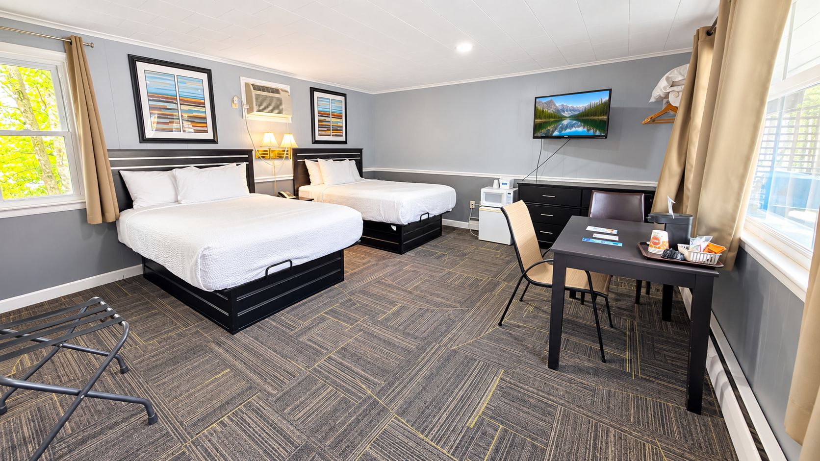 Une chambre d’hôtel avec deux lits, un bureau, une chaise, une télévision et une fenêtre avec des rideaux.