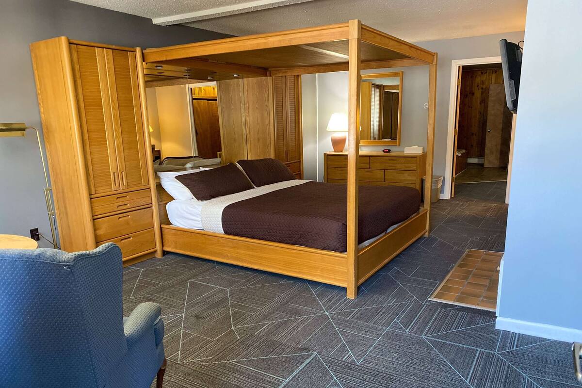 Ein Schlafzimmer mit Himmelbett, Holzschrank, Nachttisch, Lampe und einem Spiegel.