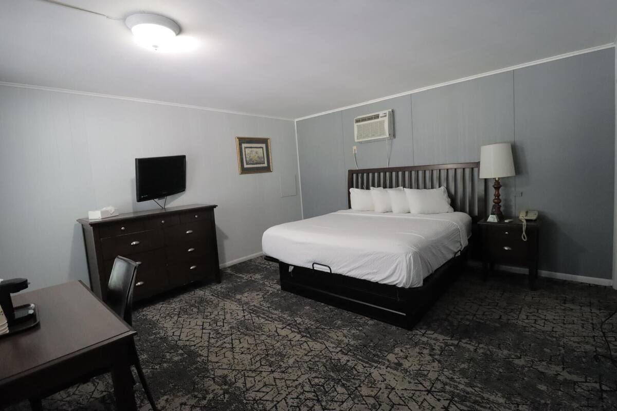 Ein Hotelzimmer mit Bett, Fernseher, Kommode, Schreibtisch und Lampe.