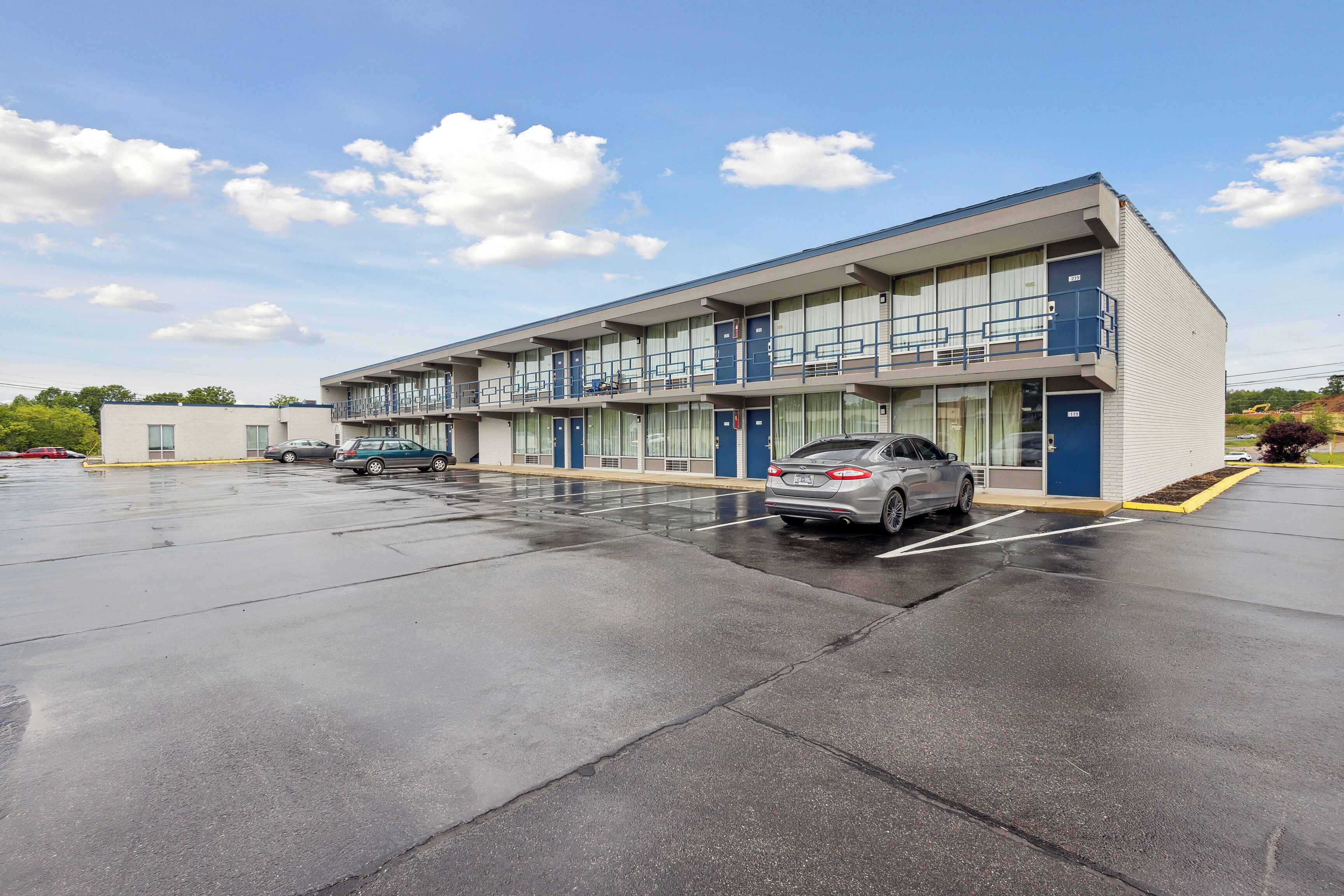 Un motel moderno con struttura su due piani, diverse camere e un parcheggio.