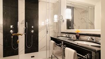 Un baño moderno con dos cabinas de ducha de mármol negro, ducha con mampara de vidrio, tocador doble y un espejo grande.