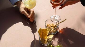 A table with two drinks, a bowl of peanuts, and a bowl of olives.