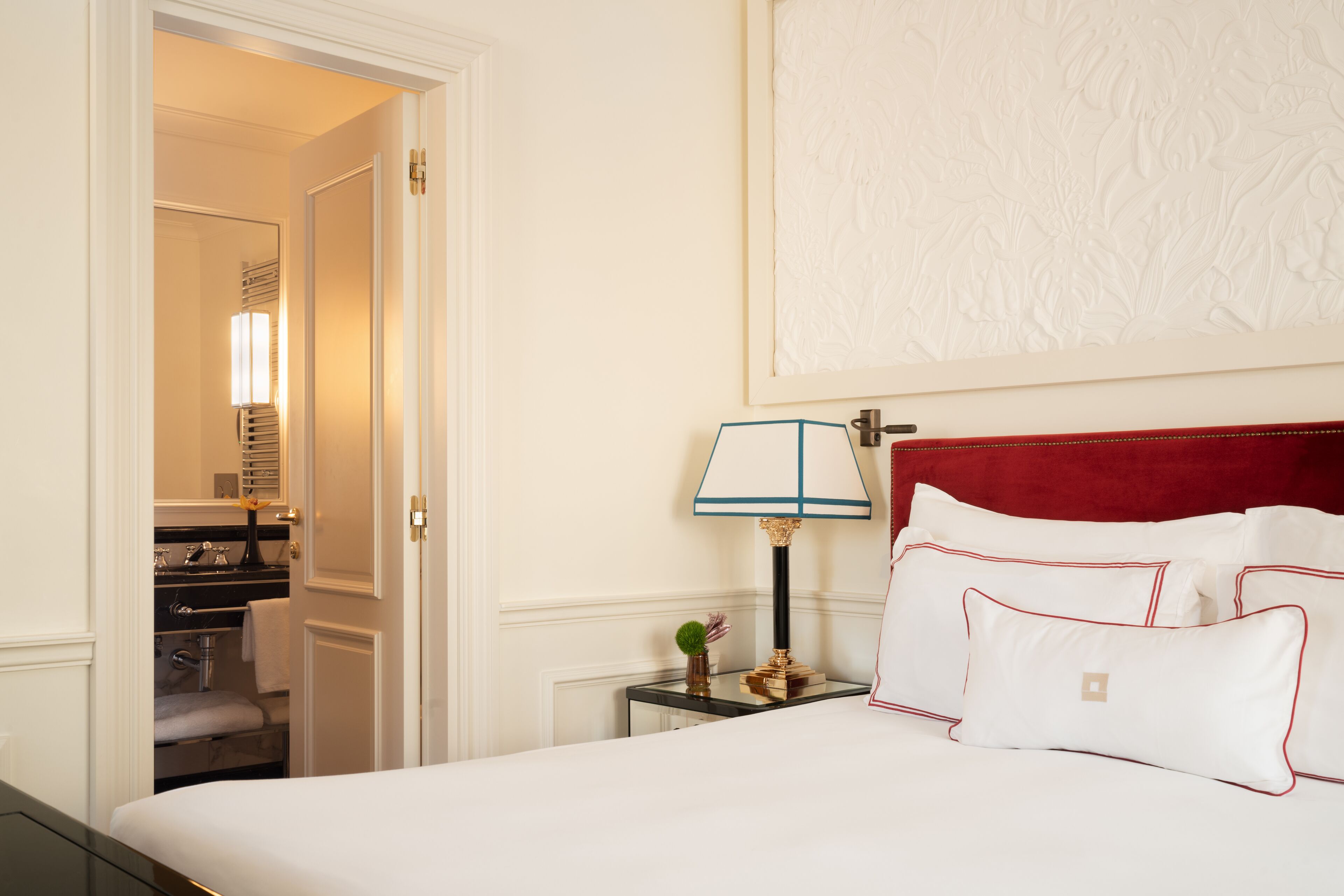 Ein Hotelzimmer mit einem ordentlich bezogenen Bett, einer Nachttischlampe und einem roten Kopfteil.
