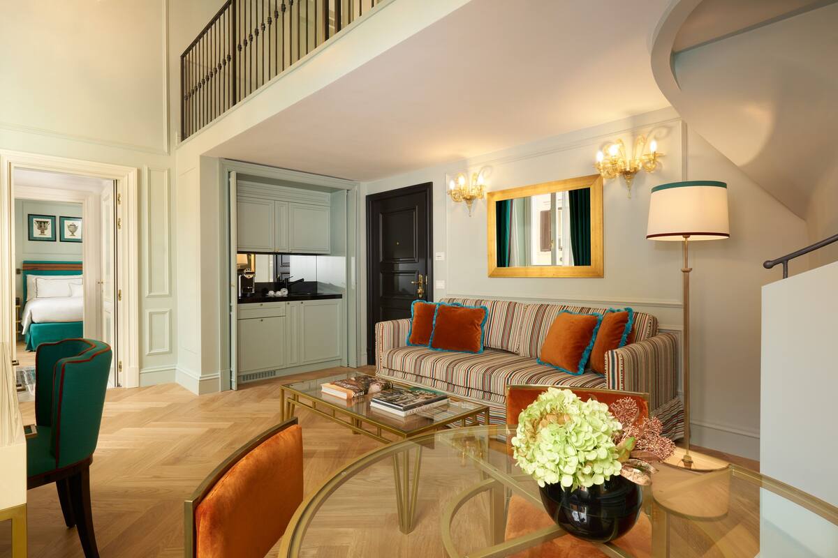 A spacious living area with a sofa, coffee table, and chairs. A kitchen is visible in the background.