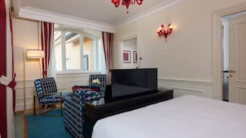 A hotel room with a large bed, a TV, a desk, and two patterned chairs.
