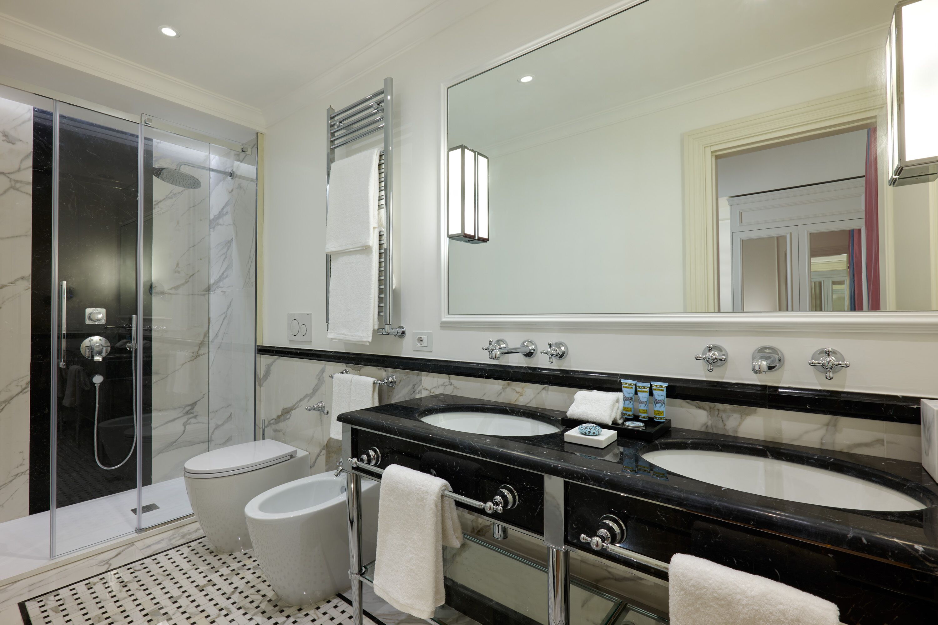 A modern bathroom with two sinks, a glass shower enclosure, and a large mirror.