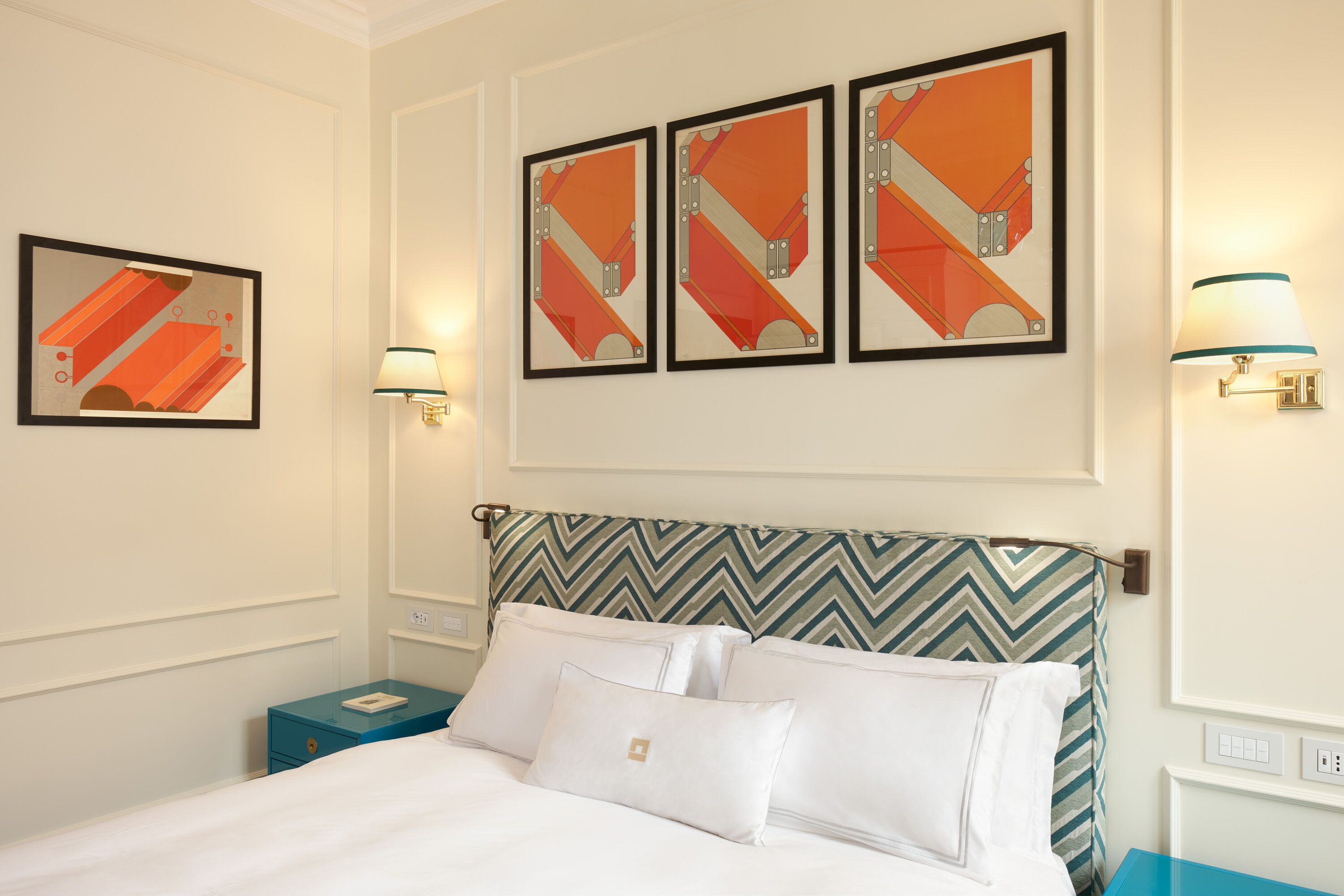 Habitación de hotel con una cama, una mesita de noche, una lámpara y tres cuadros enmarcados en la pared.