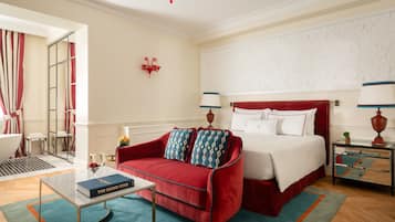 A hotel room with a red sofa, a bed with white bedding, a small table with a book, and a nightstand with a lamp.