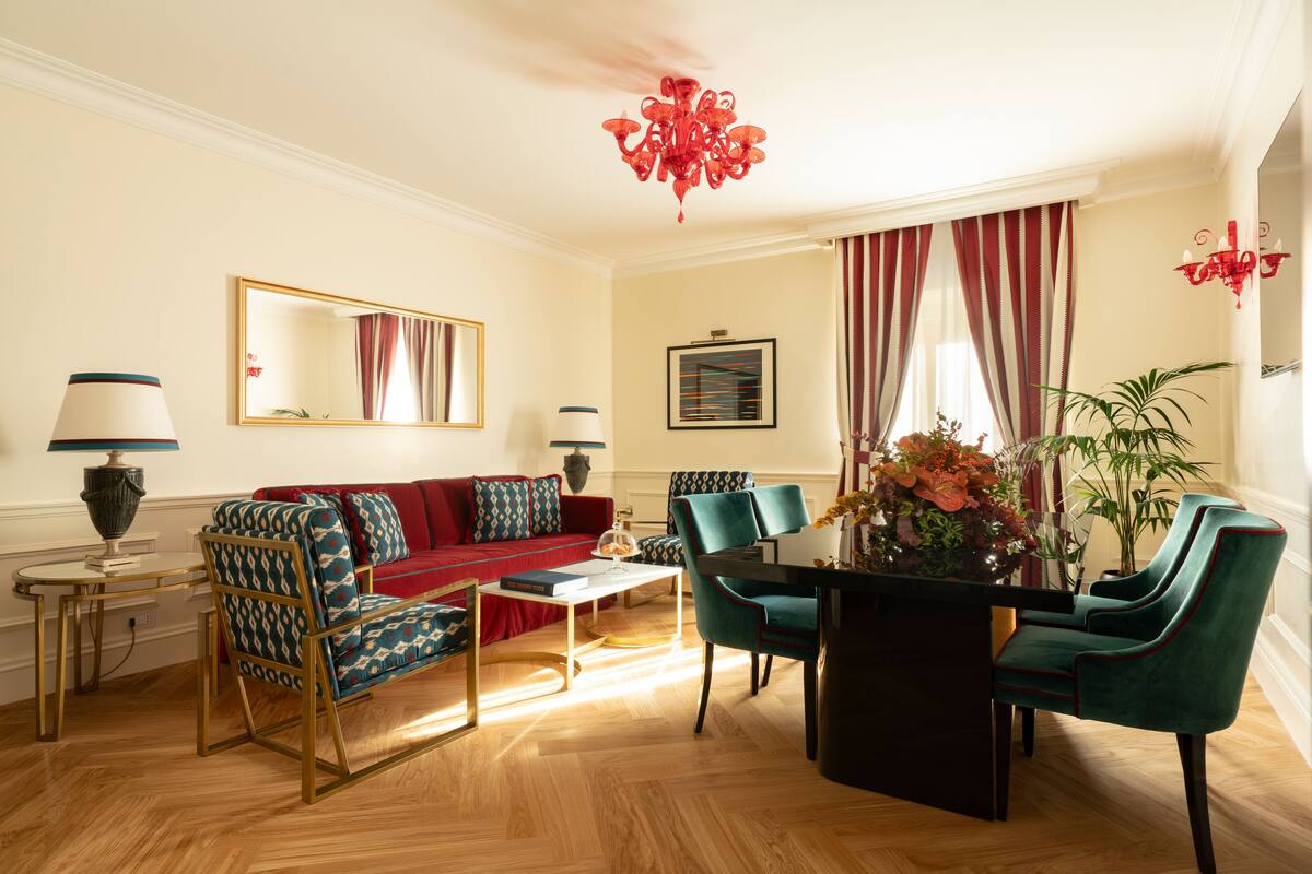 A living room with a red sofa, teal chairs, a coffee table, and a chandelier.
