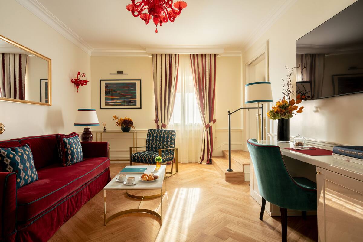A living room with a red sofa, teal armchair, and a coffee table with a book and pastries.