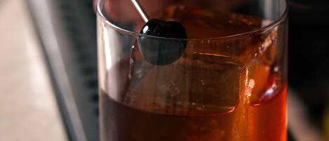 Un bicchiere trasparente con un liquido scuro, probabilmente un cocktail, e un cucchiaino appoggiato sul bordo.