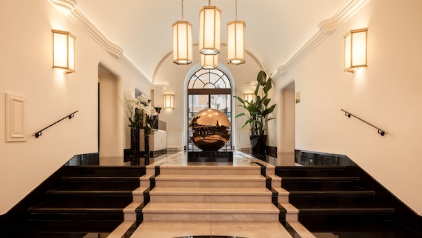 A grand hallway with a marble staircase, wall sconces, and a large decorative bowl at the top. - Palazzo Ripetta (Rome)