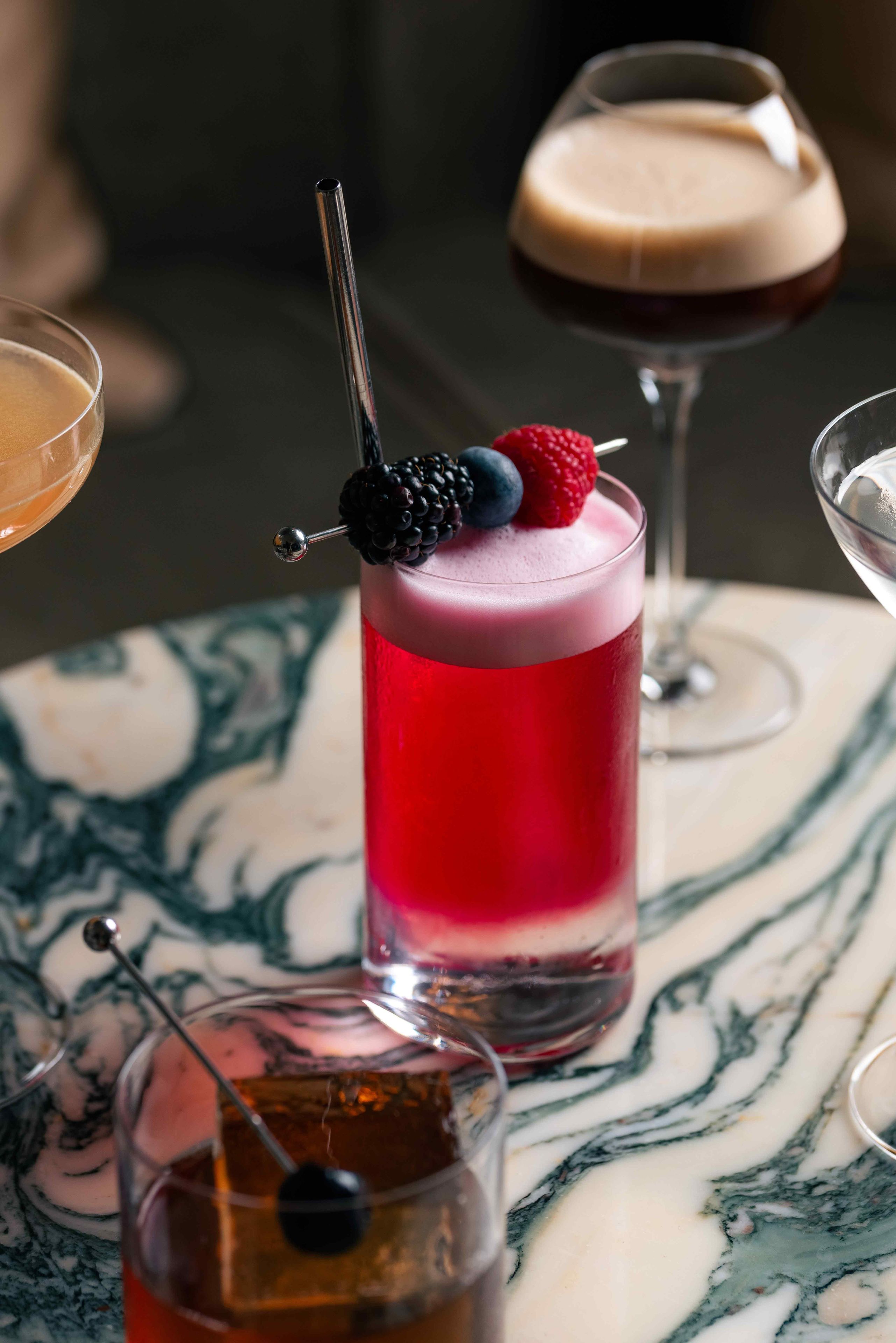 A glass with a layered drink and a blackberry on a marble table.