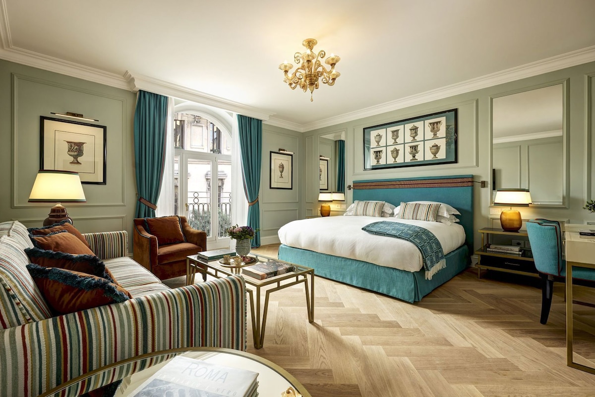A hotel room with a bed, a sofa, a coffee table, and a chandelier.